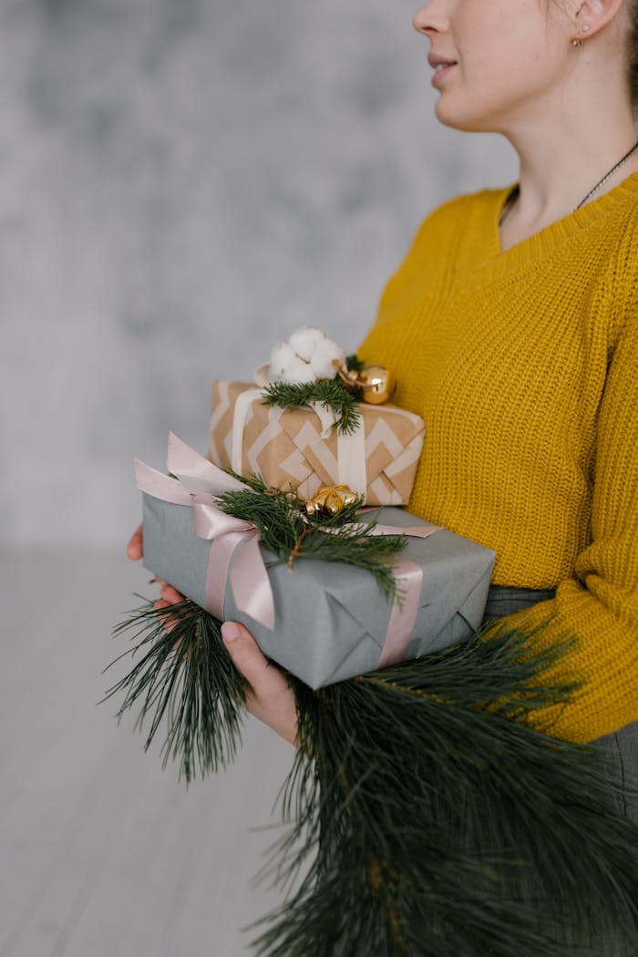 A woman in a yellow sweater holds Christmas presents decorated with pine branches and ribbons.