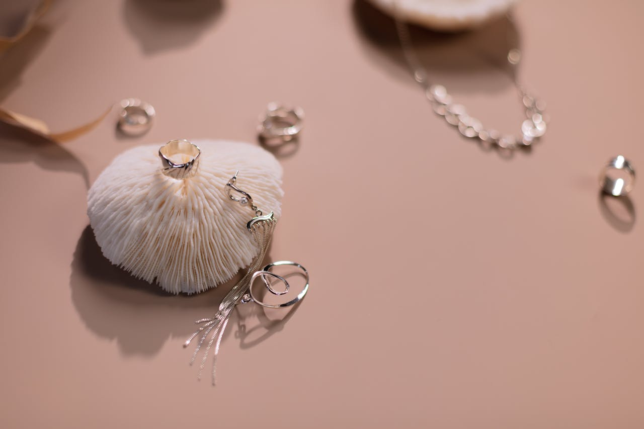 Stylish silver rings and necklace displayed artfully on a soft pink background.